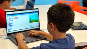 A young boy codes on a laptop, focused on a block-based programming interface.