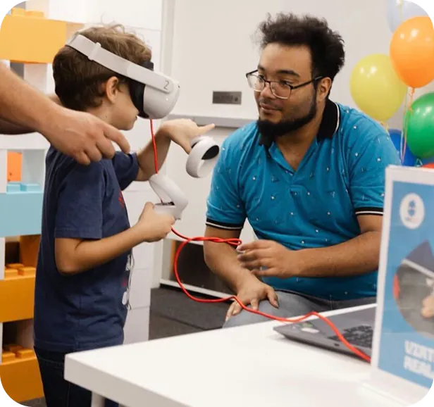 A young boy experiences virtual reality with a headset and controllers, guided by an adult.