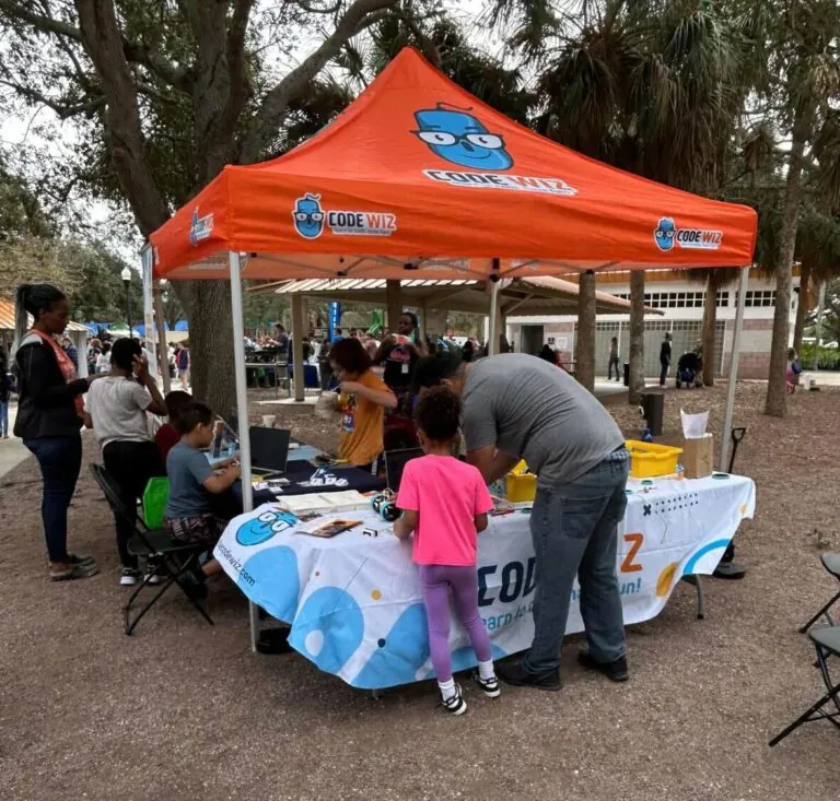 Children and adults learn coding and robotics at an outdoor Code Wiz event booth.