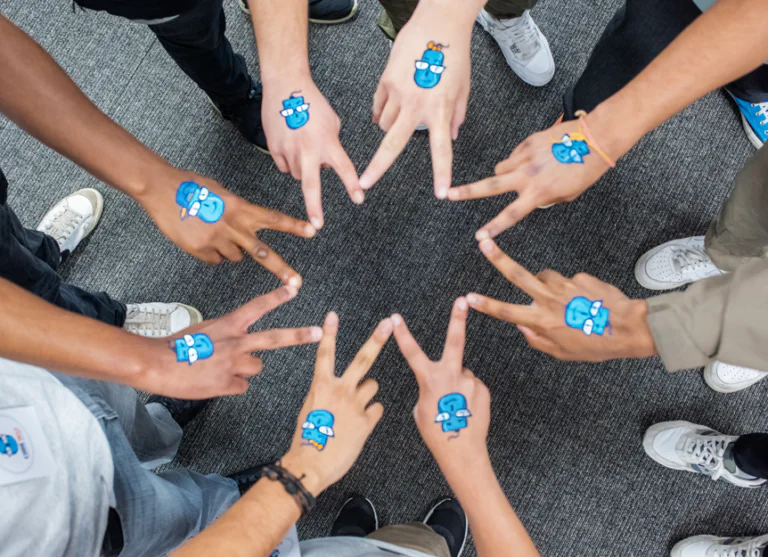 Diverse hands adorned with blue cartoon tattoos form a star pattern on a grey carpet. TITLE