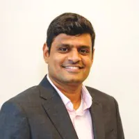 Smiling professional man in a dark suit and pink shirt looks directly at the camera. TITLE