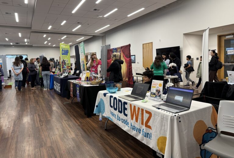 Attendees explore educational booths, including a prominent "Code Wiz" display with laptops, at a bustling