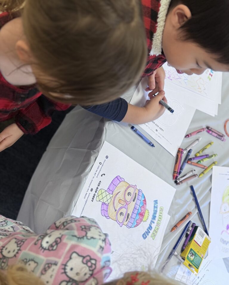 Two children color character drawings and logos with crayons on a table. TITLE:
