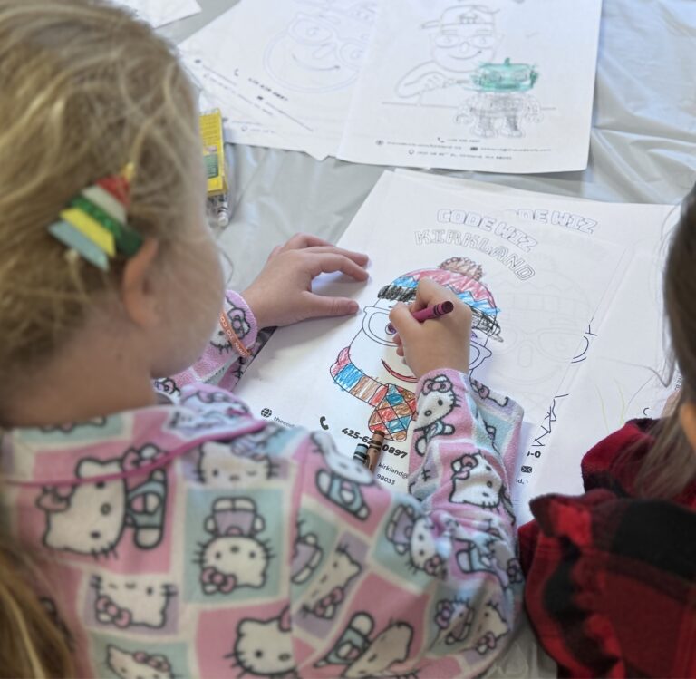 A child in Hello Kitty pajamas colors a character on a 'Code Wiz Kirkland' coloring page.