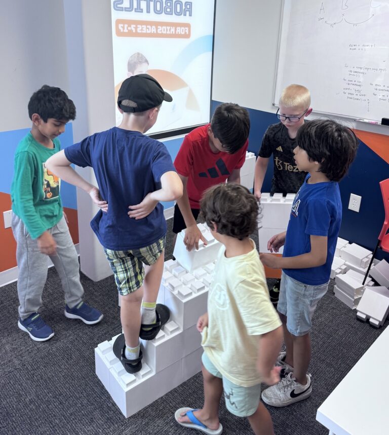 Young boys collaboratively building a structure with giant white blocks at a STEM center.