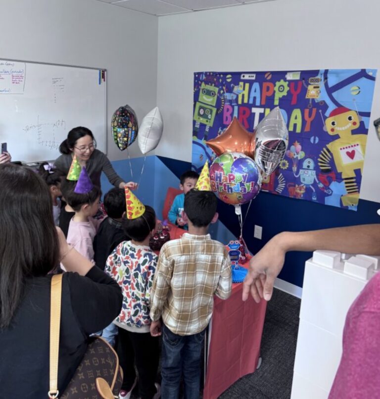 A woman helps children at a robot-themed birthday party with balloons and a banner.