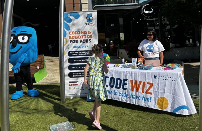 A Code Wiz booth with a mascot and staff engages a child in outdoor coding and robotics activities.