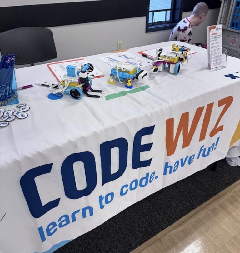 A Code Wiz table displays colorful robots and coding materials for learning.