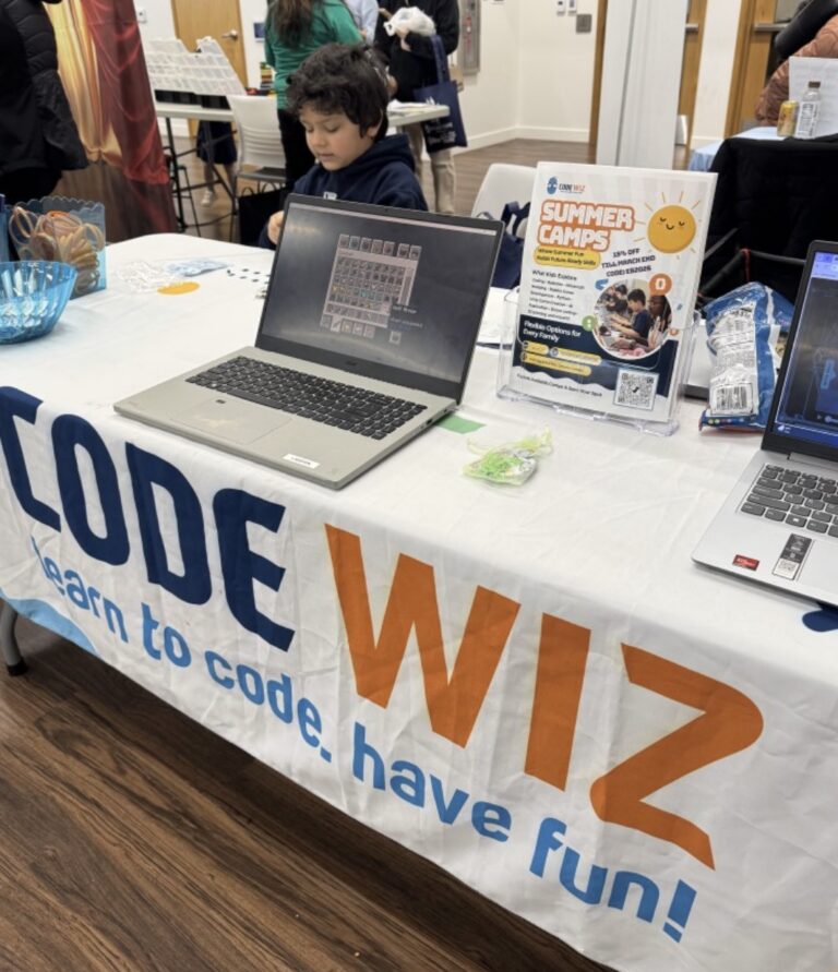 A boy engages with a laptop at a Code Wiz booth promoting summer coding camps. TITLE: