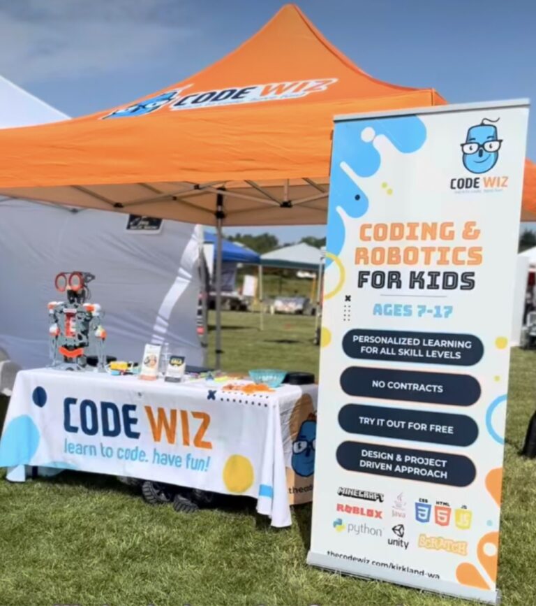 An outdoor Code Wiz booth with an orange tent, robot, and banner promoting coding