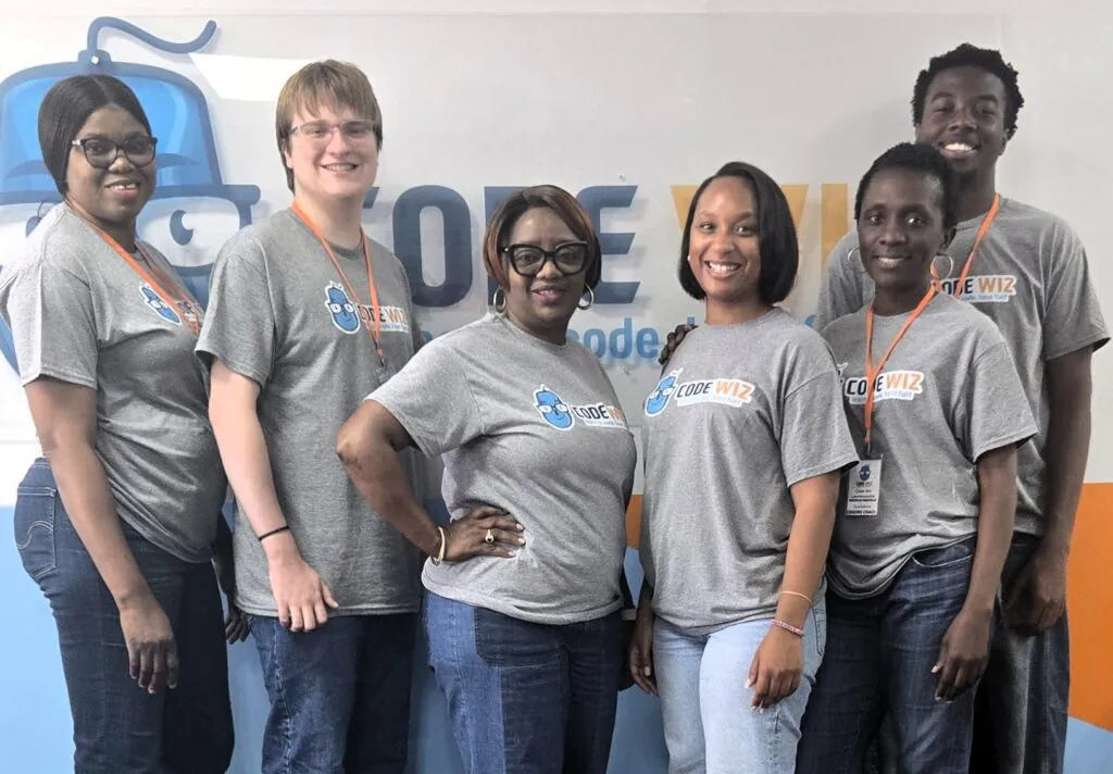 Six smiling Code Wiz team members in gray t-shirts stand together.