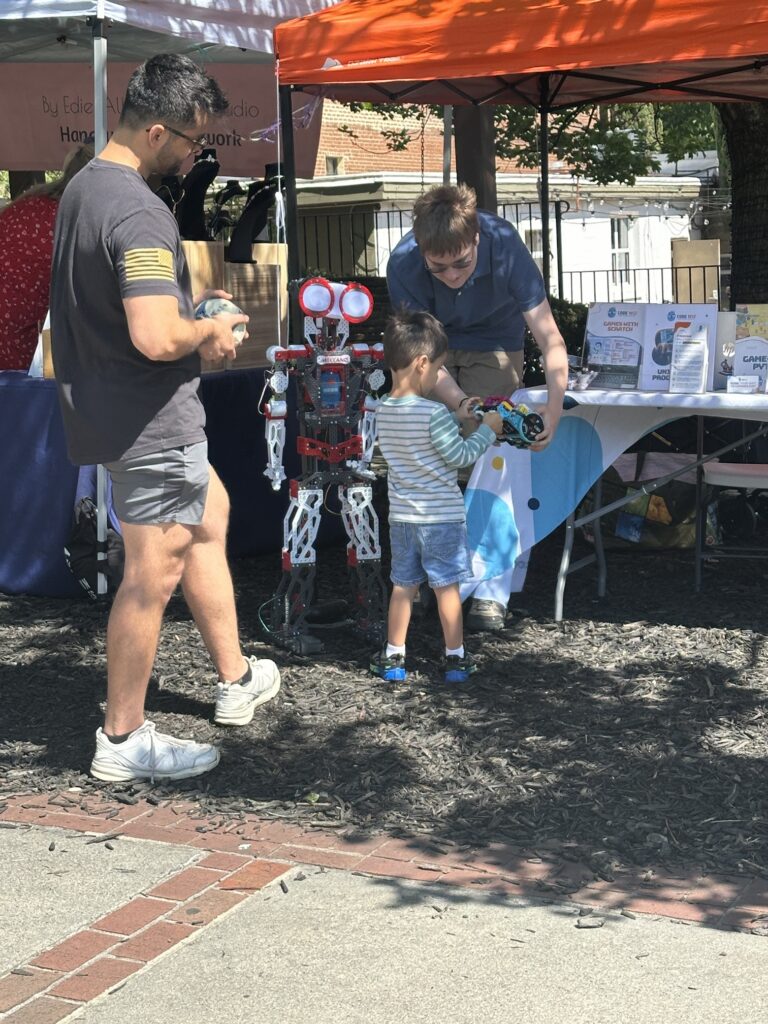 A young boy and an adult explore robotics at an outdoor educational event.