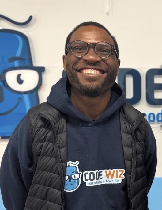 A smiling man wearing glasses and a Code Wiz hoodie stands in front of the brand