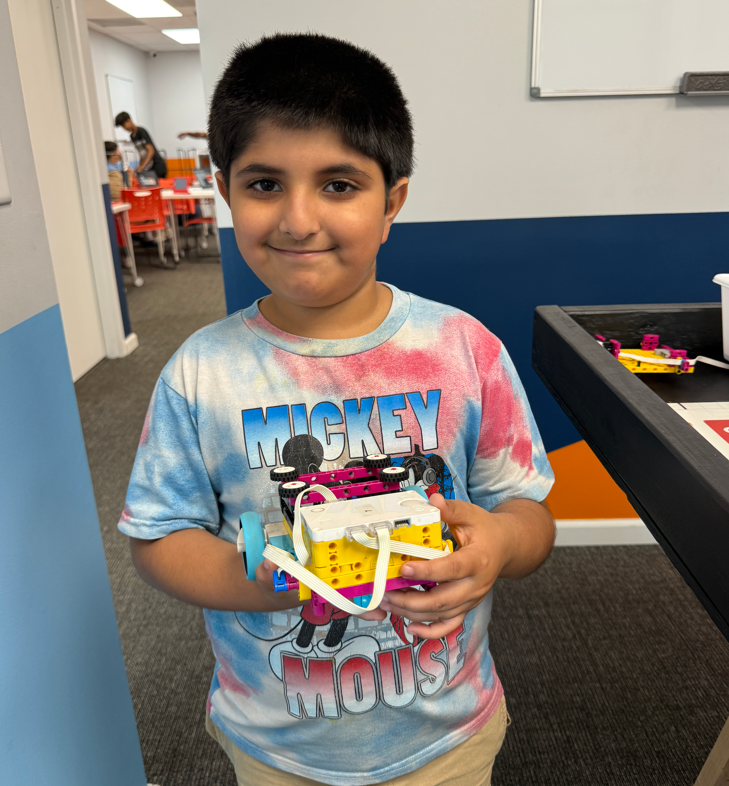 A young boy proudly displays his colorful Lego robot in a STEM classroom.