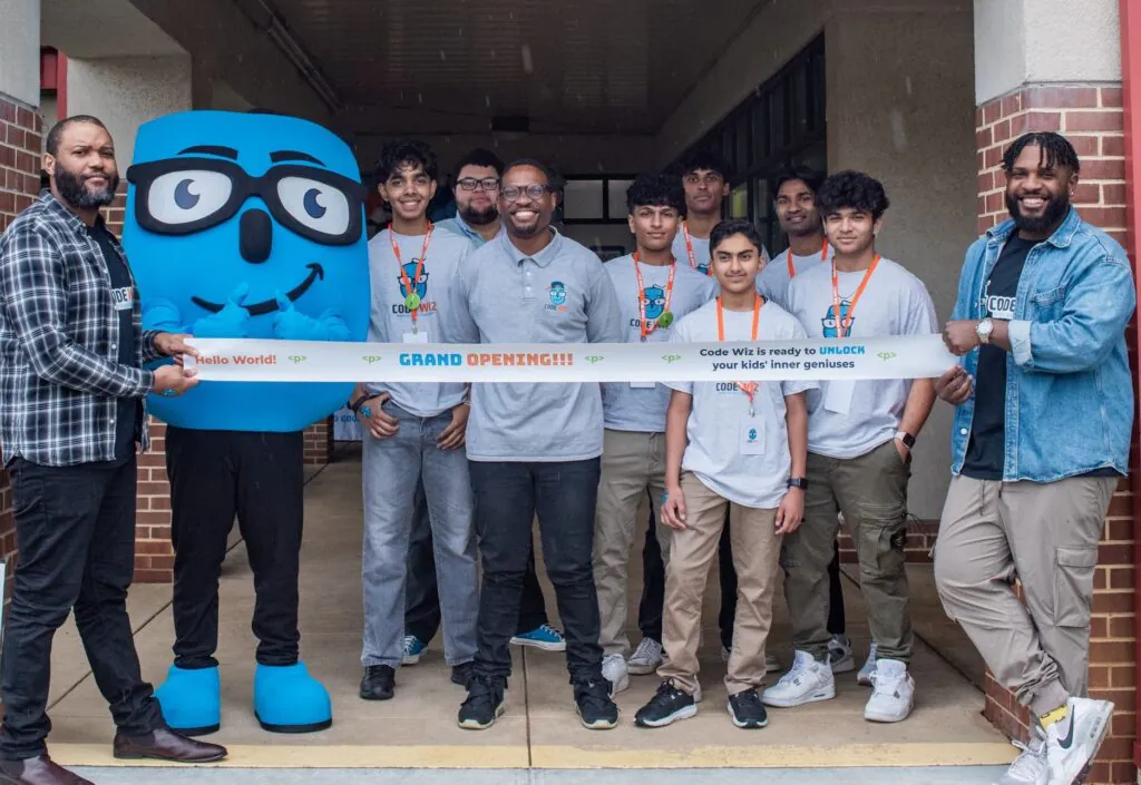 Code Wiz grand opening celebration with smiling staff, students, and mascot. TITLE