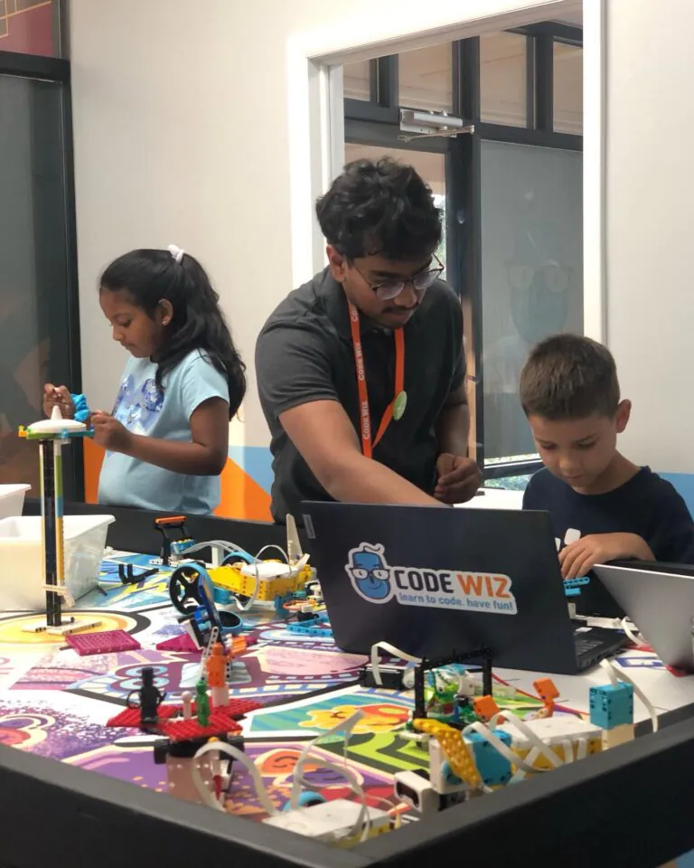An instructor guides two young students building robots and coding on laptops at Code Wiz. TITLE