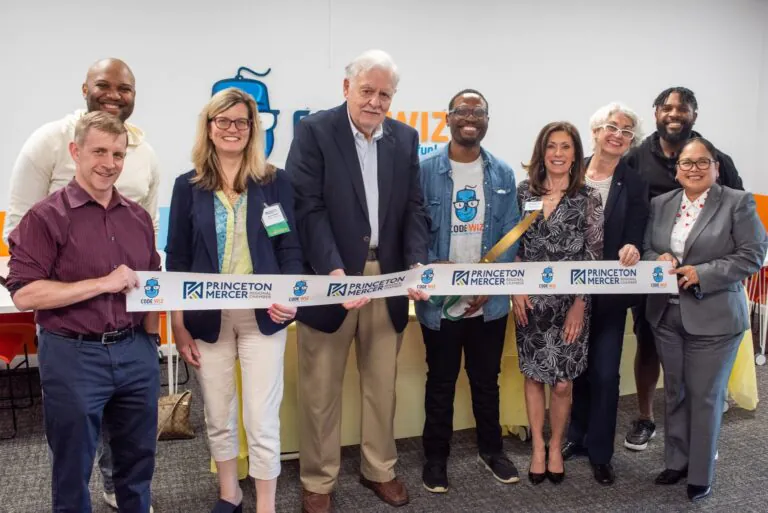 Nine diverse people smile while holding a ribbon for a Code Wiz and Princeton Mercer Chamber grand opening.