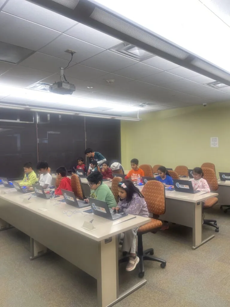 Young students engage in a coding class, working on laptops with an instructor present.