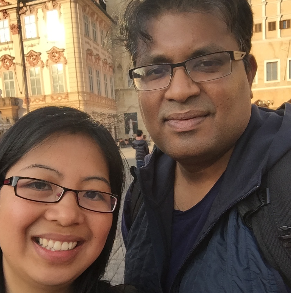 A smiling woman and man pose for a selfie in front of historic European buildings.