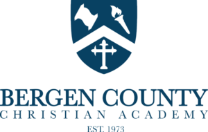 Bergen County Christian Academy logo featuring a shield with a scroll, torch, and cross