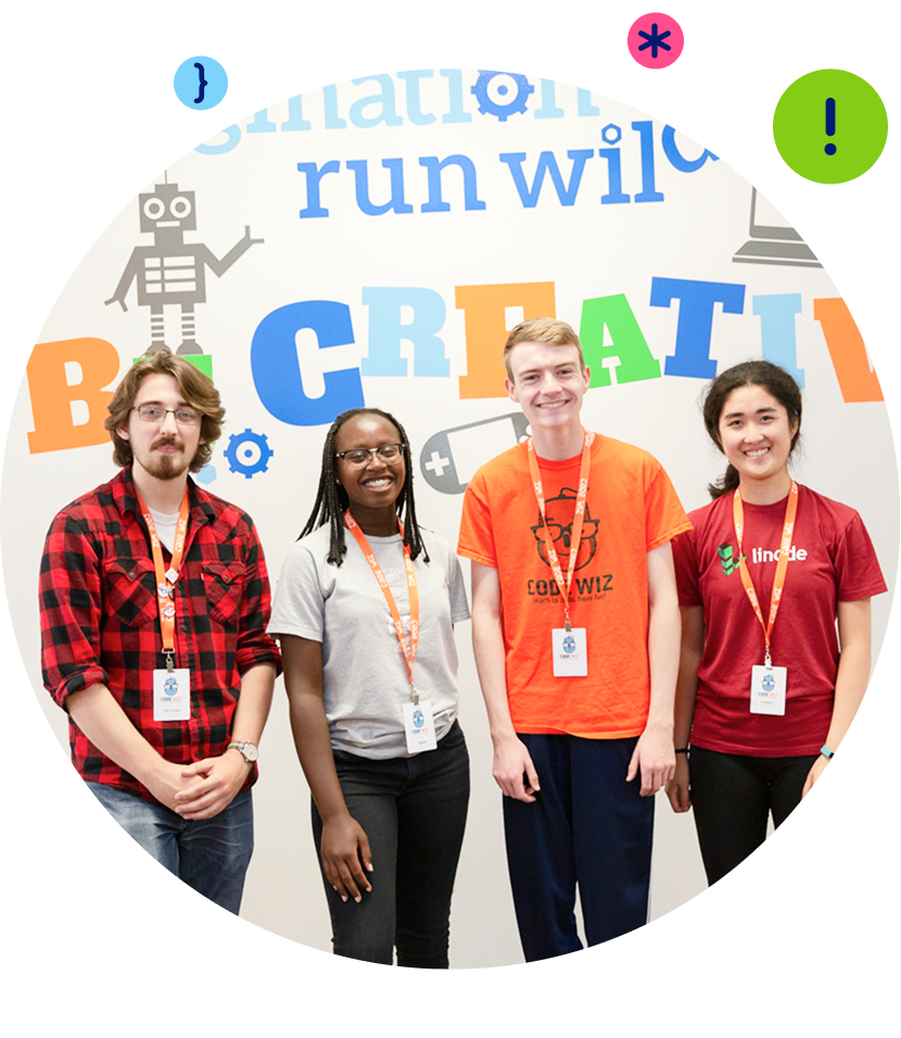A diverse group of four smiling students wearing lanyards stands before a colorful "Be Creative