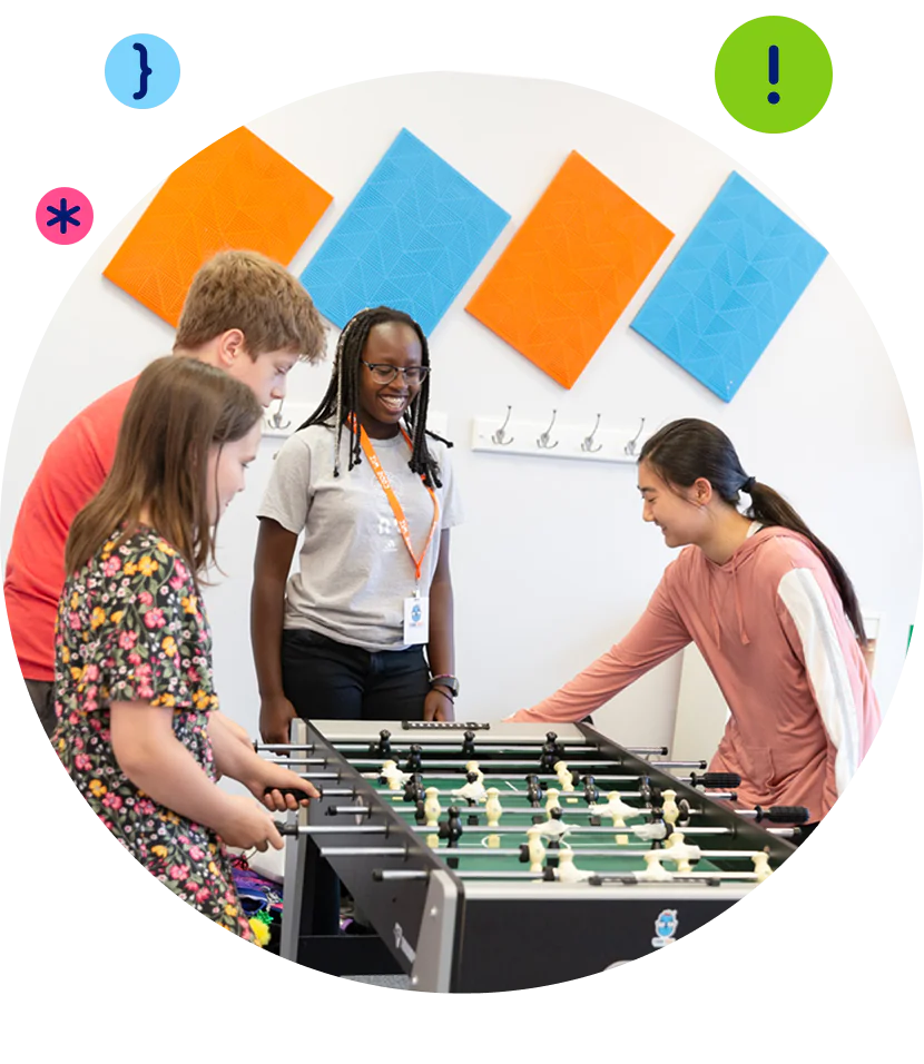 Four diverse young people happily play a game of foosball in a bright, modern room.