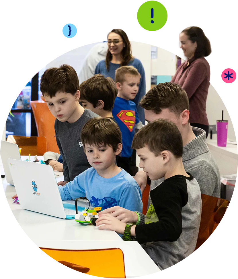 Young students and instructors collaborate on coding projects with laptops and robots.