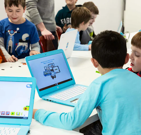 Children intently use blue laptops for a LEGO Education activity in a bright classroom. TITLE