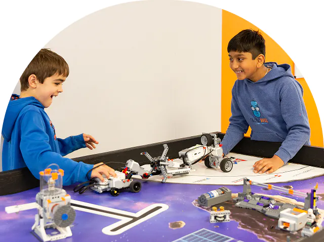 Two smiling boys excitedly operate robots on a space-themed mat. TITLE: