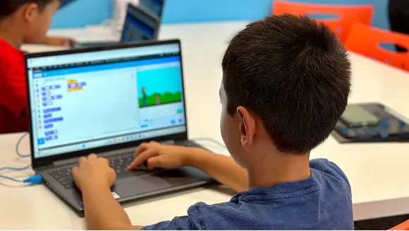 A young student learns coding on a laptop, displaying a visual block-based programming interface.