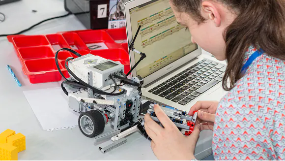 A young person programs and builds a Lego Mindstorms robot using a laptop. TITLE