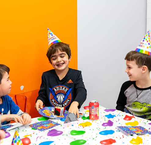 Kids in birthday hats enjoy cake and drinks at a festive party.