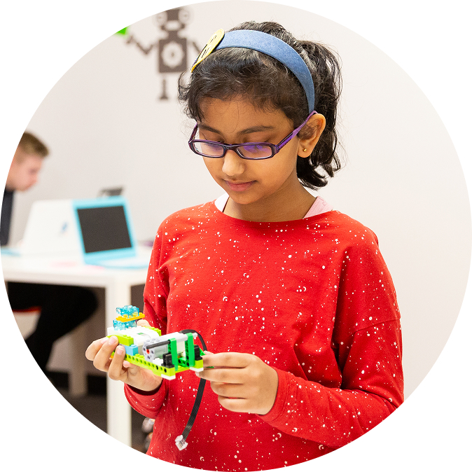 A focused girl in glasses and a red shirt intently examines a colorful robot built from bricks.