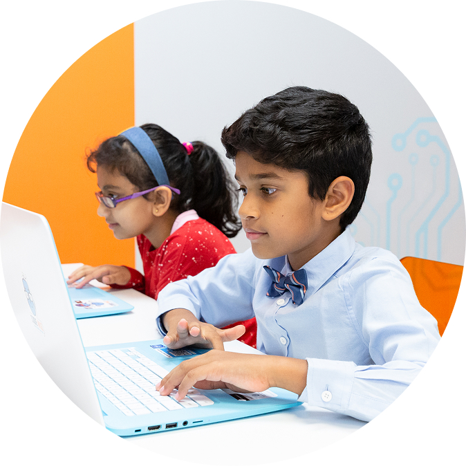 Two young students intently type on light blue laptops in a bright, modern classroom.