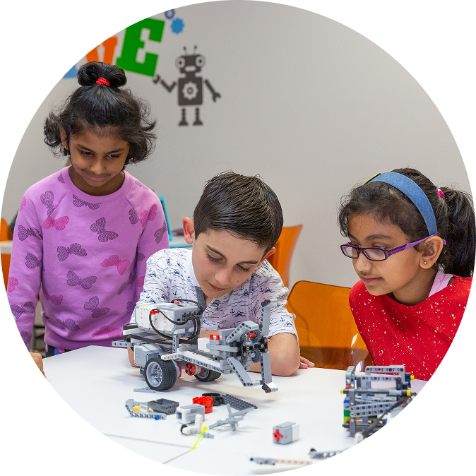Three children intently build a robot with building blocks, engaged in a STEM learning activity. TITLE