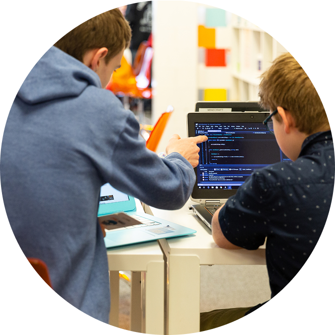 Two students collaborate on a coding project, with one pointing at the laptop screen. TITLE