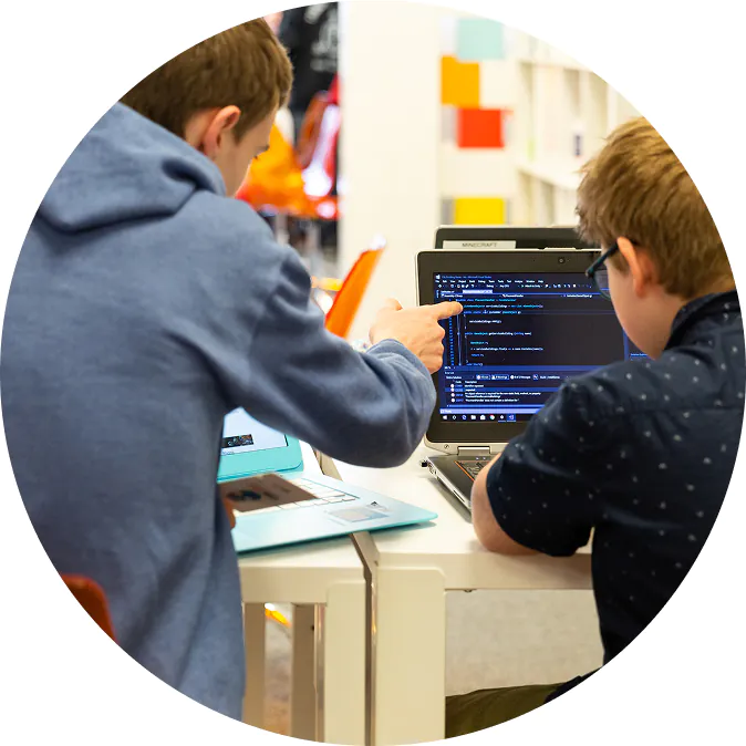 Two students collaborate on a coding project, with one pointing at the laptop screen. TITLE